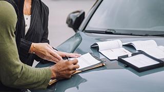 Två personer skriver avtal på motorhuven på en bil.